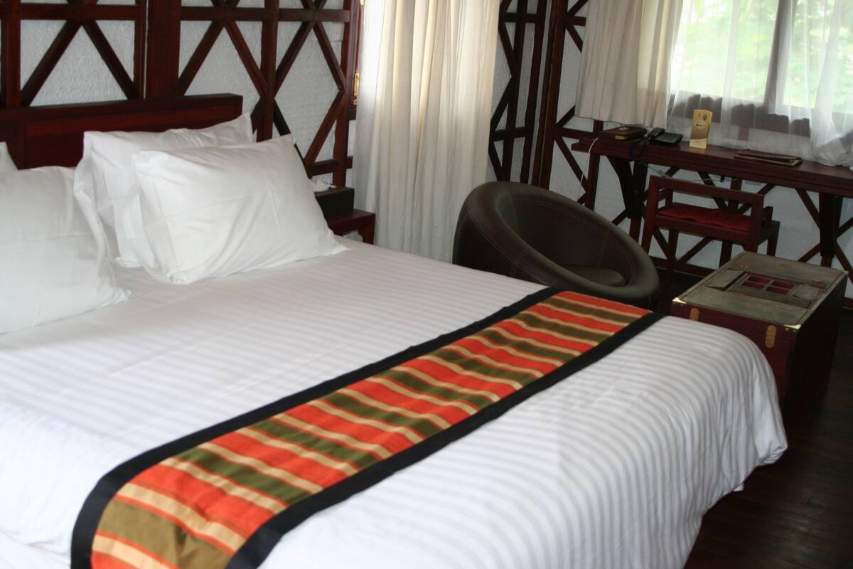A hotel room with a bed, a desk, a chair, and a window with curtains.