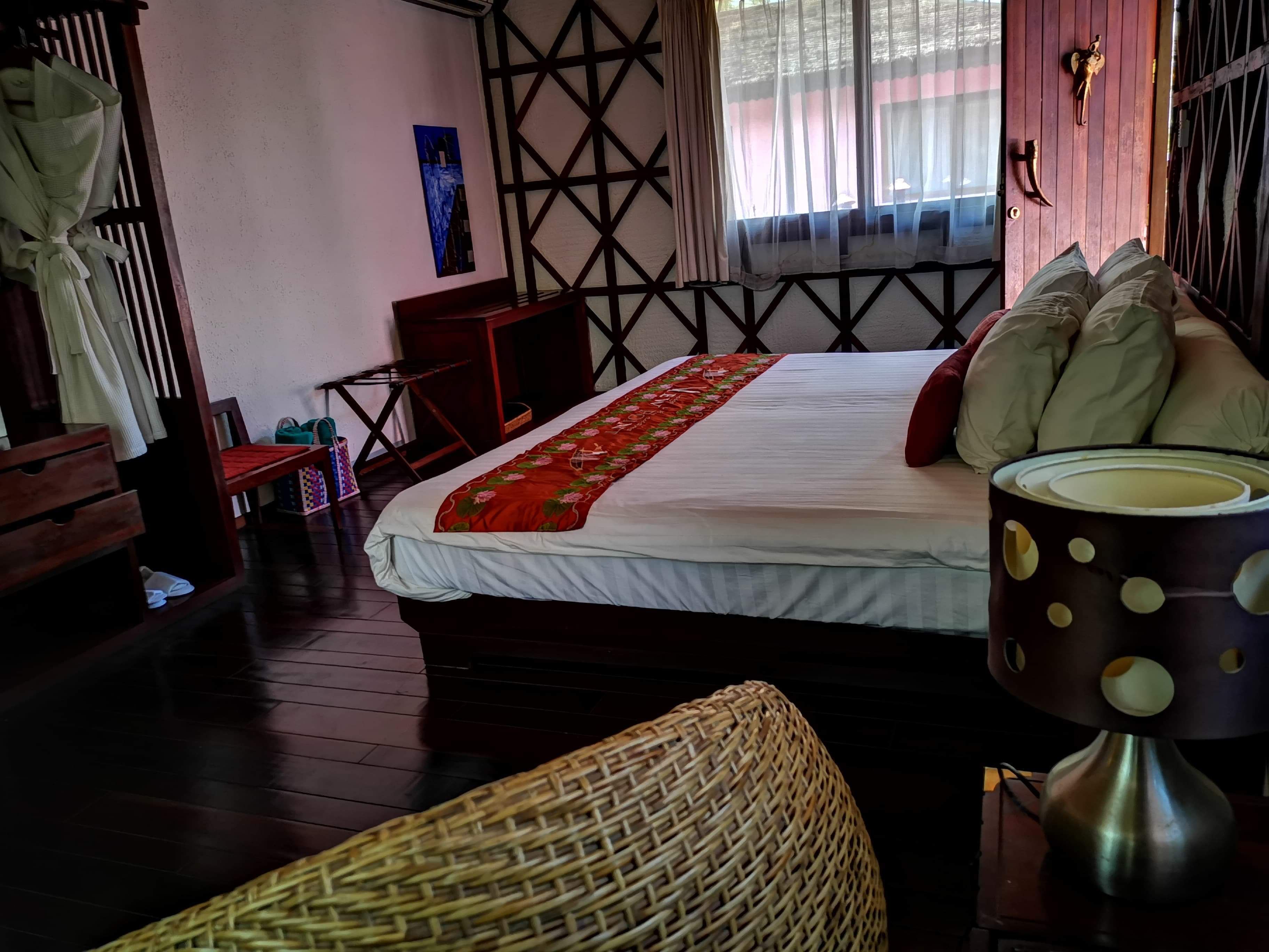 A neatly arranged hotel room with a bed, a bedside lamp, a woven basket, and a wooden chair.