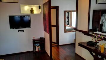 Habitación de hotel con televisor de pantalla plana, estantería, taburete de madera, espejo y ventana con vistas al exterior.