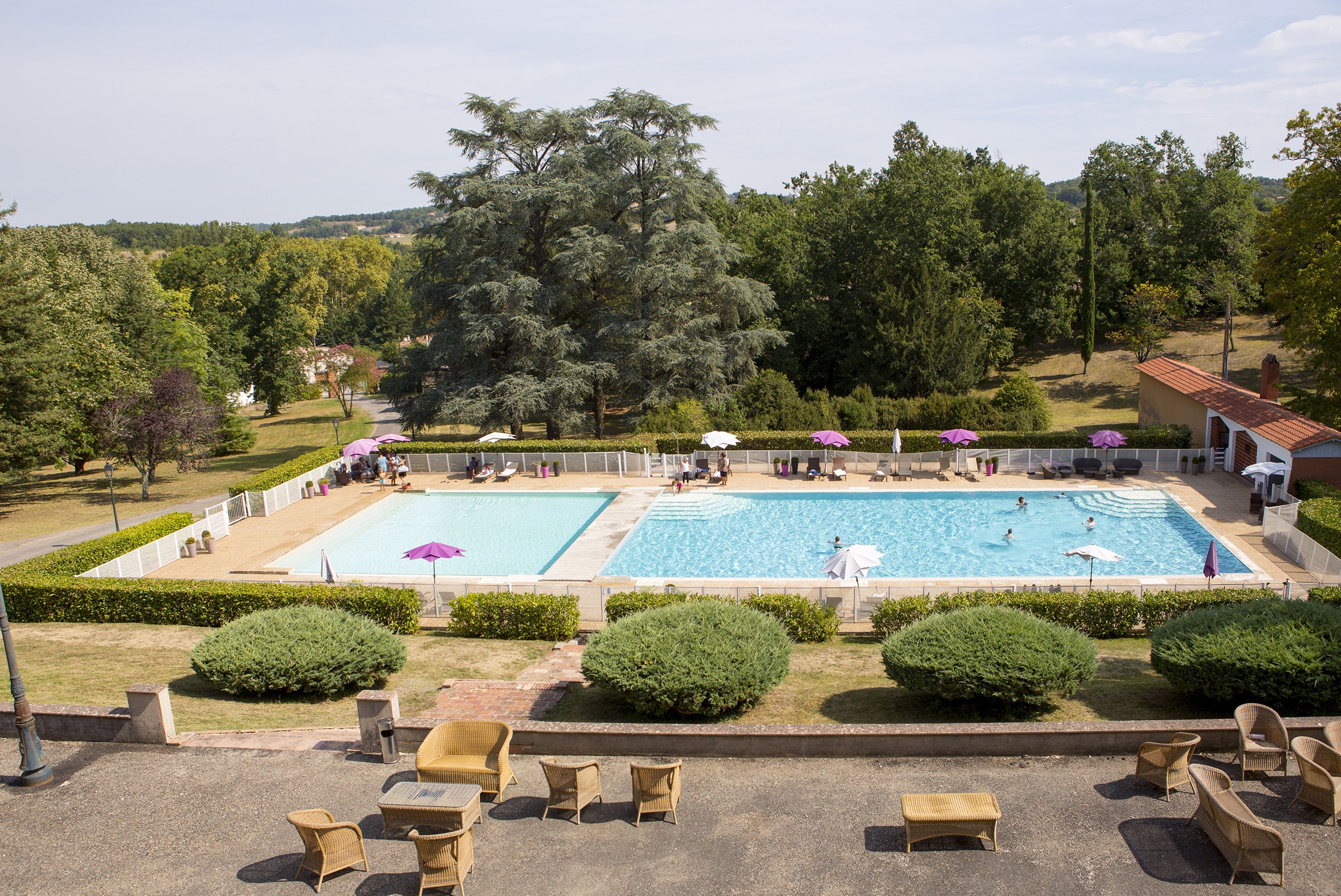 A large outdoor swimming pool with multiple lanes, surrounded by well-maintained lawns and hedges.
