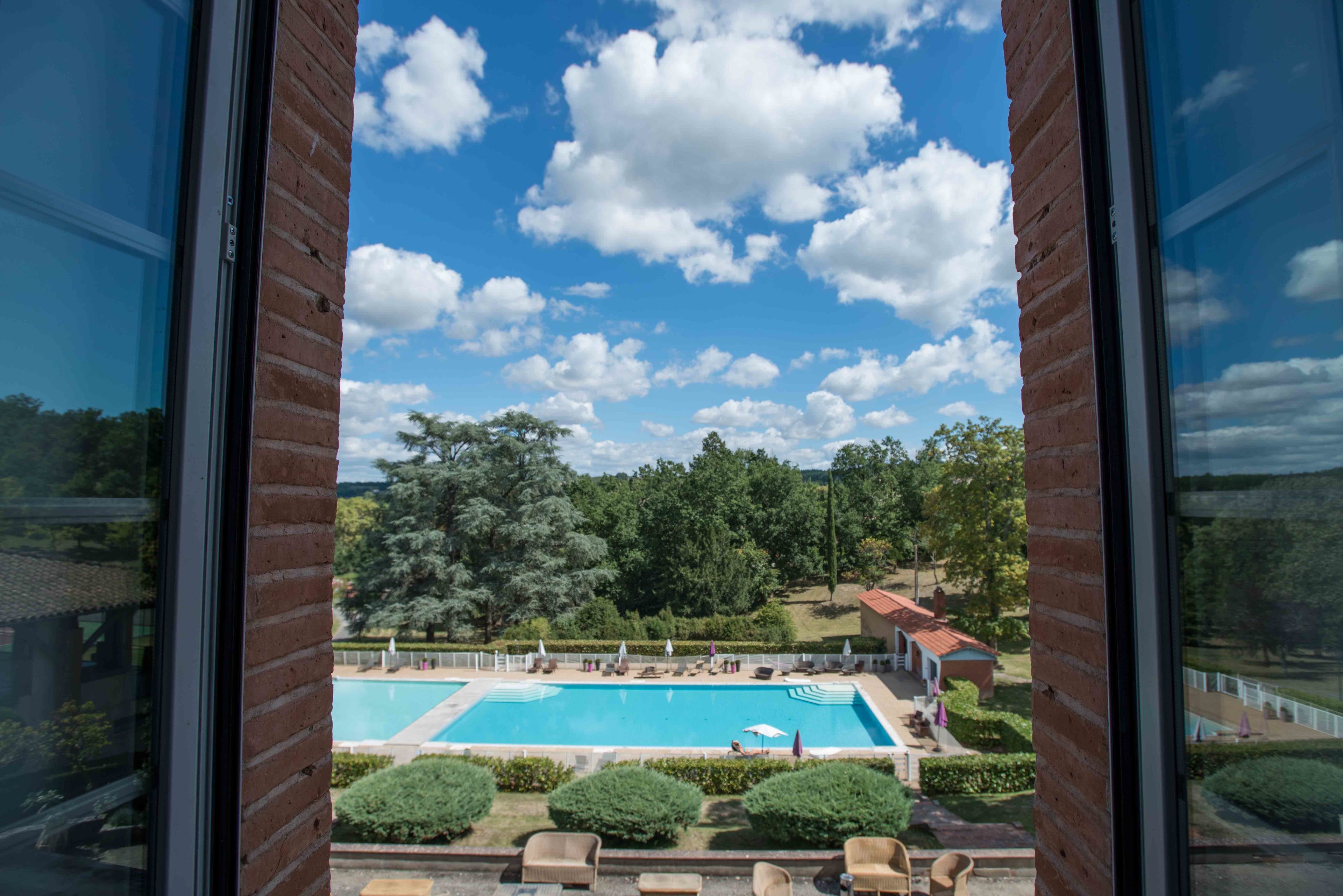 Vista de una piscina con sillas de descanso y sombrillas, rodeada de follaje y árboles.