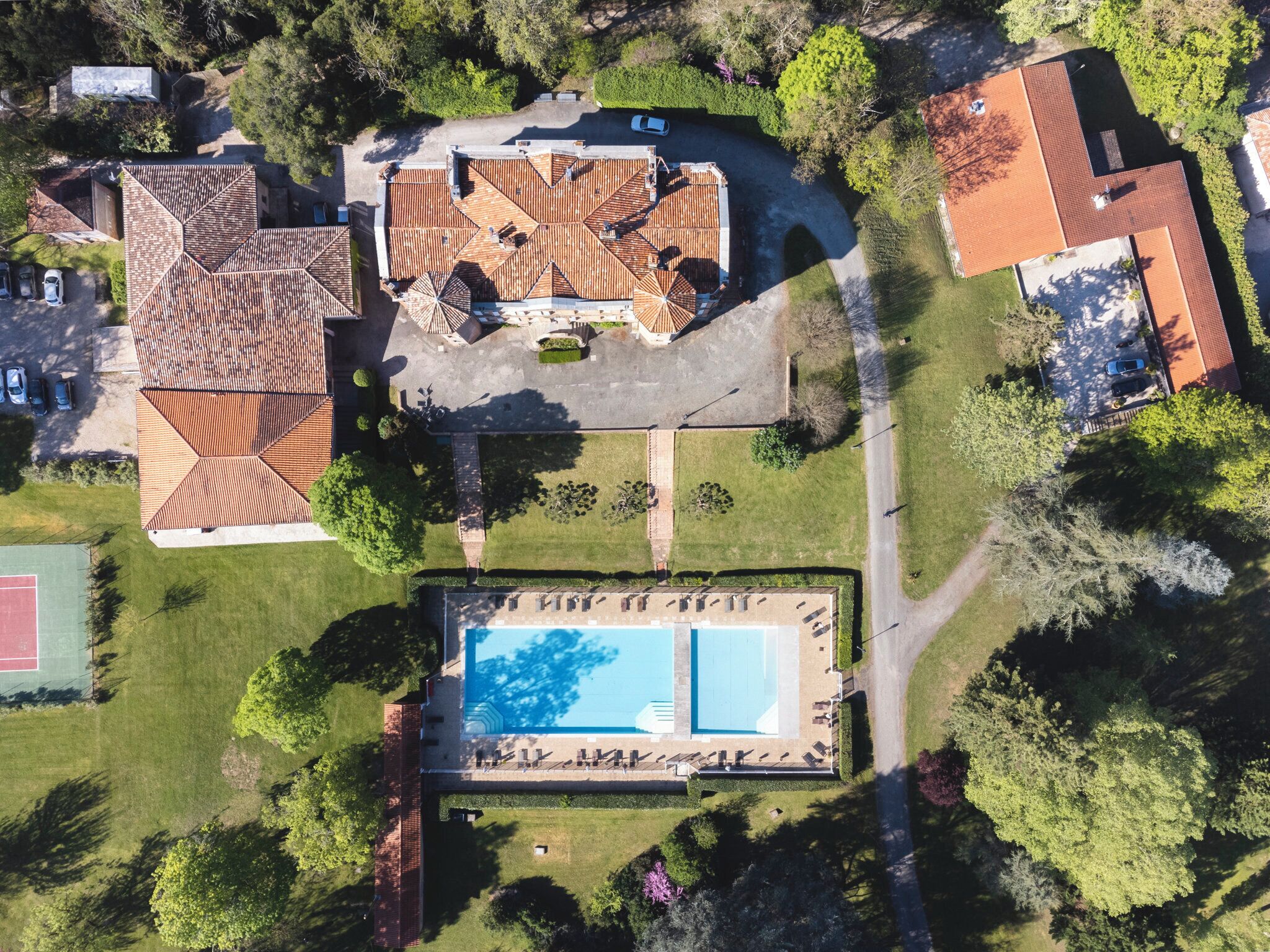 An aerial view of a residential area with a swimming pool, a tennis court, and a house with a tiled roof.