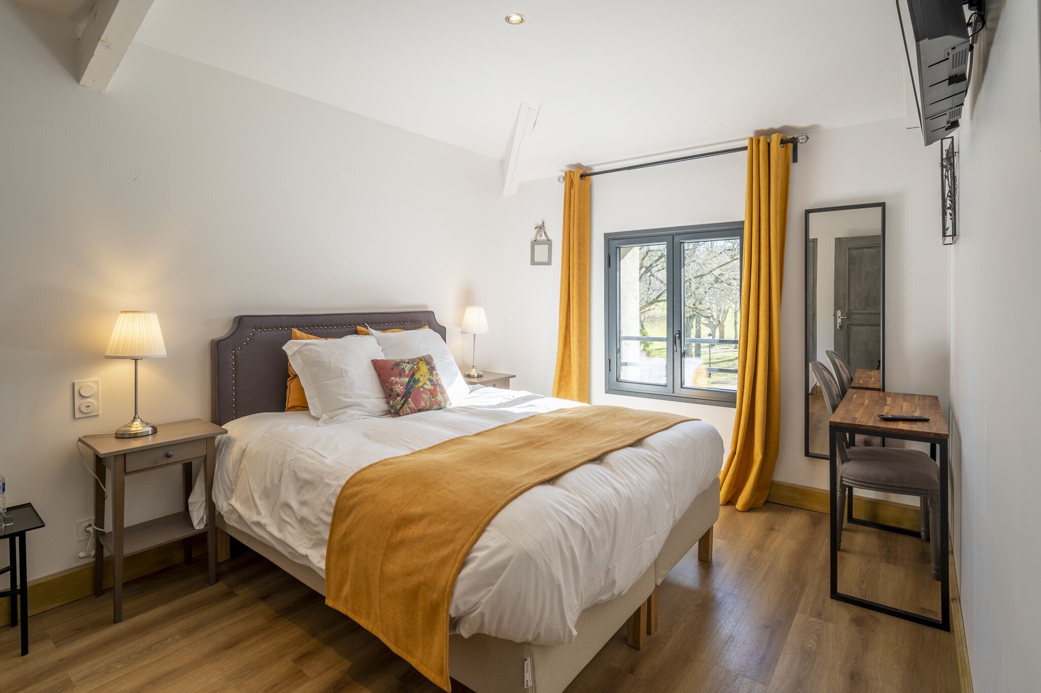 A bedroom with a bed, bedside lamps, a window with curtains, a wooden table, and a chair.