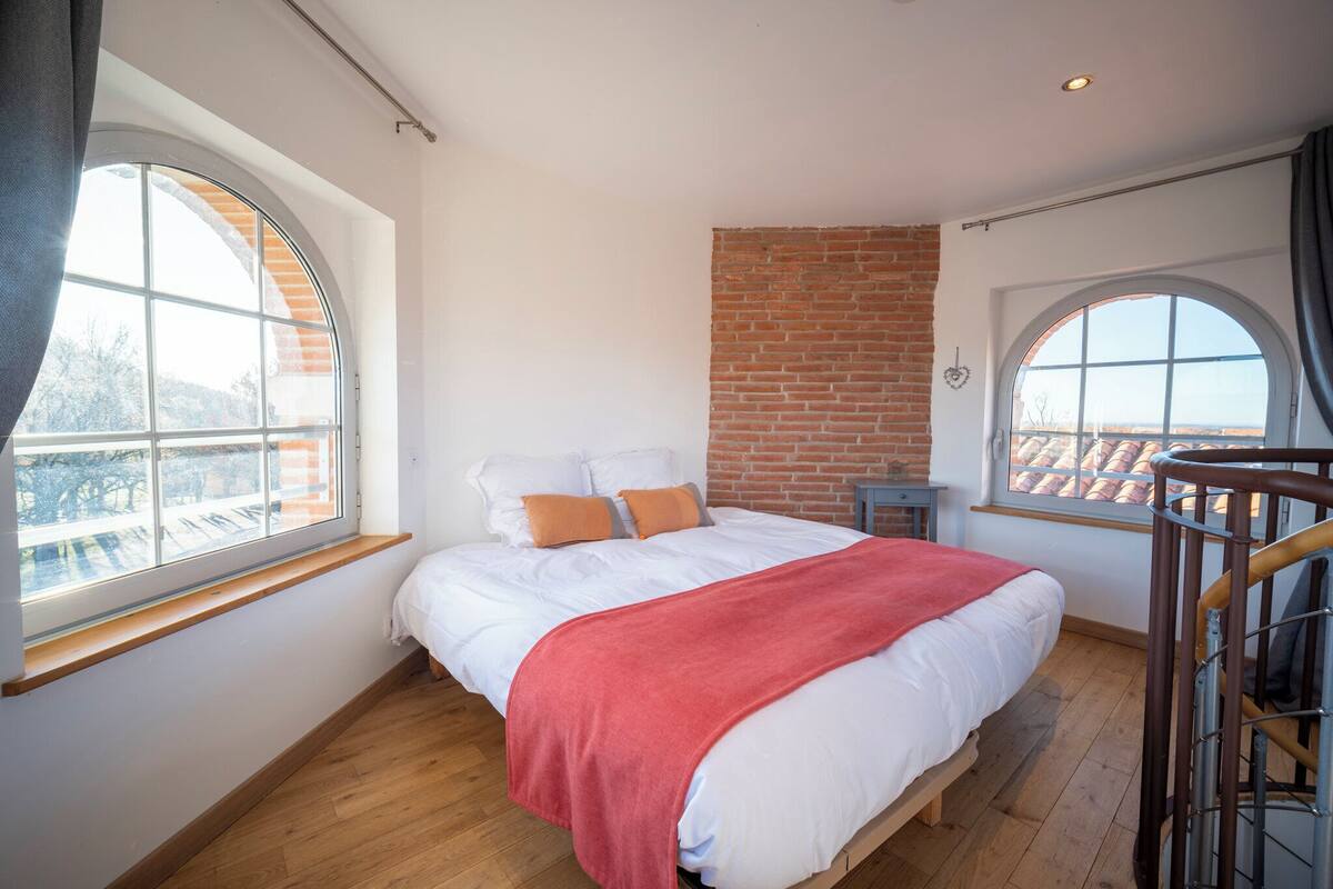 Une chambre avec un grand lit, un mur en briques et une vue par la fenêtre.