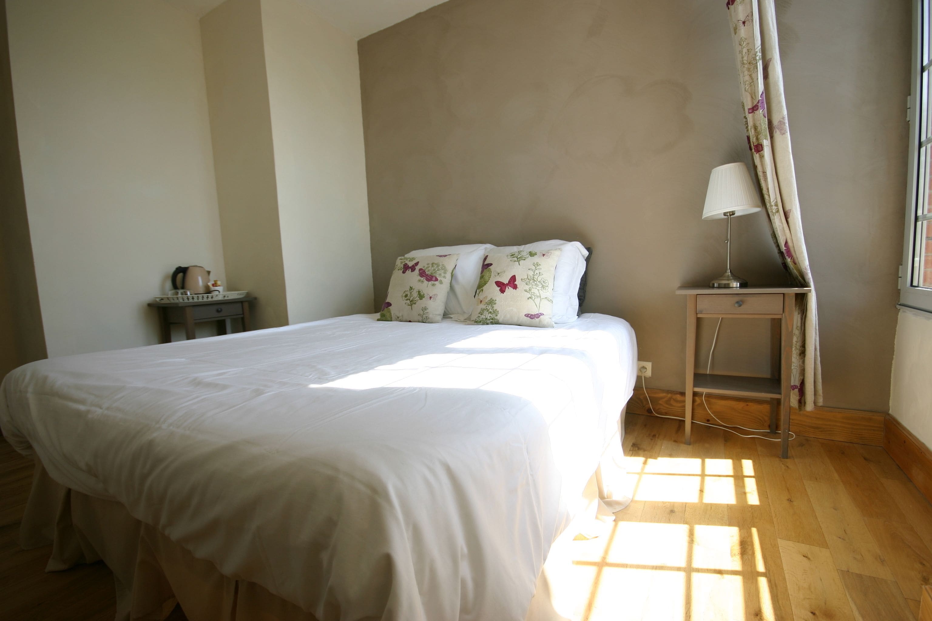 A bedroom with a large bed, a bedside table with a lamp, and a window with curtains.