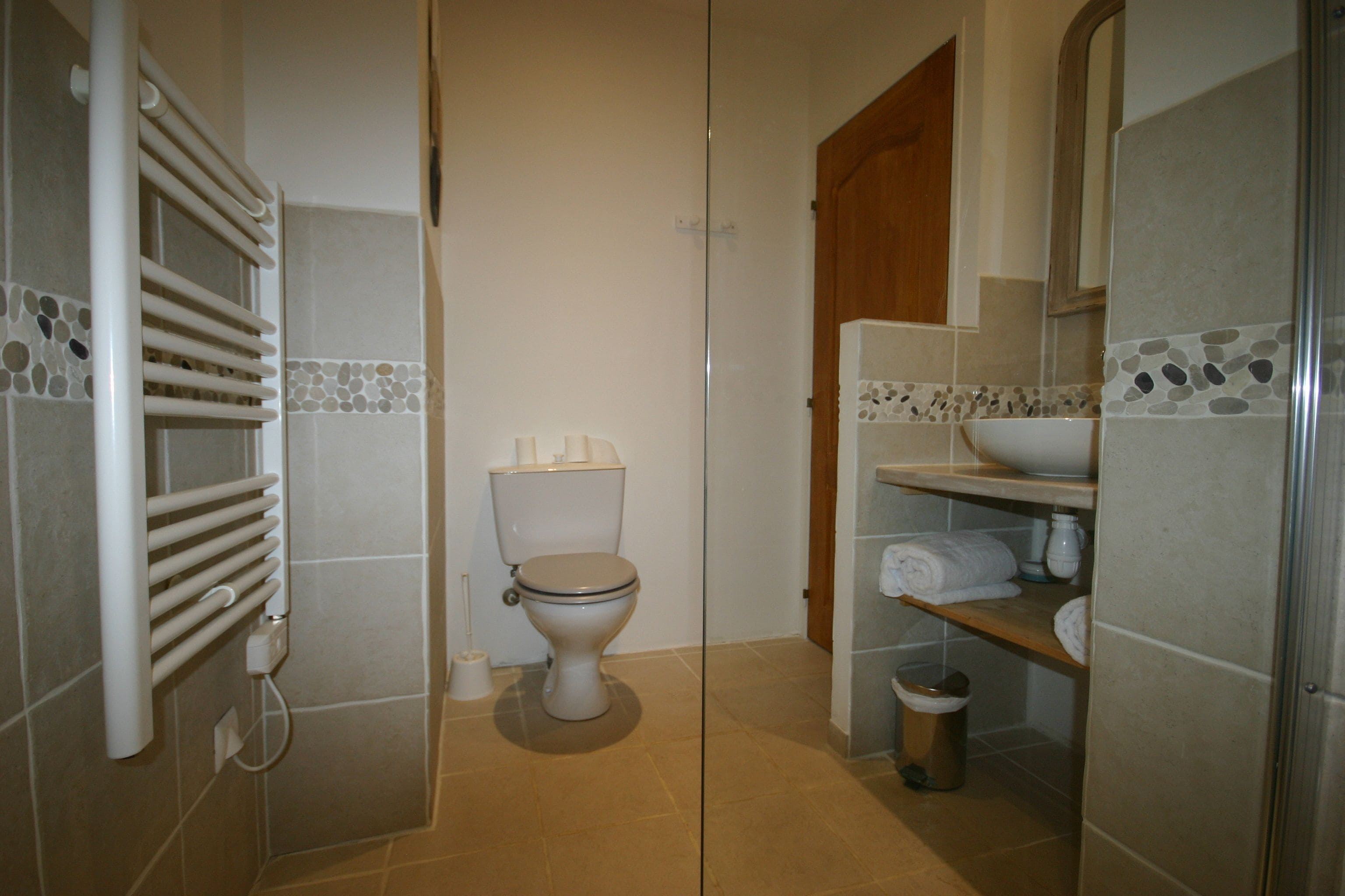 Een badkamer met een toilet, een handdoekhouder, een plank met handdoeken en een prullenbak.