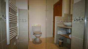 Une salle de bain comprenant des toilettes, un porte-serviettes, une étagère avec des serviettes et une poubelle.