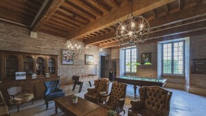 A spacious room with a pool table, leather armchairs, and a billiards table. There are wooden cabinets and a brick wall. - Château de Loubéjac (L'Honor-de-Cos)
