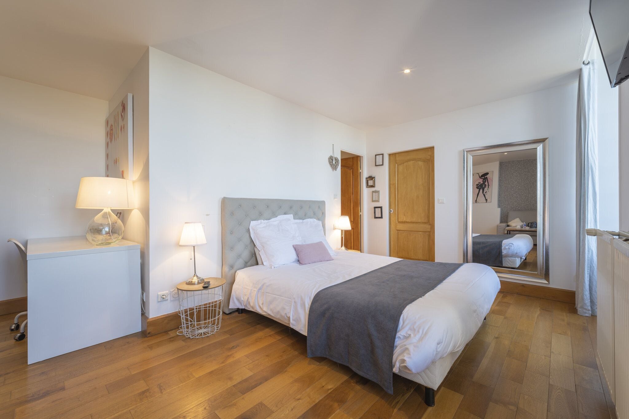 A bedroom with a bed, bedside tables, a desk, and a mirror.