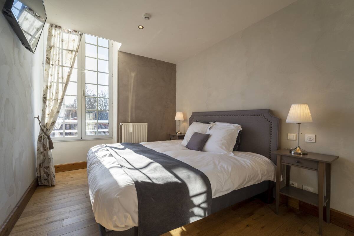 Une chambre à coucher avec un lit, deux tables de chevet avec des lampes, une fenêtre avec des rideaux et un radiateur.