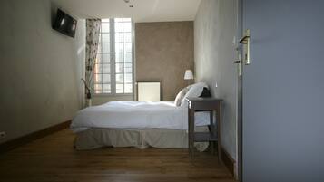 A bedroom with a bed, a nightstand, a lamp, a TV, and a window with curtains.