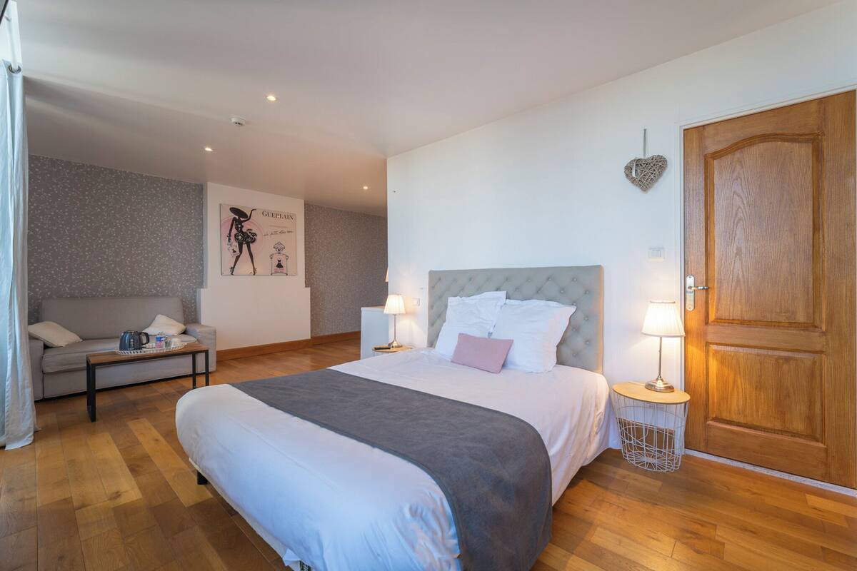 Une chambre à coucher avec un grand lit, un canapé, une petite table, une table de chevet, une lampe et une porte en bois.