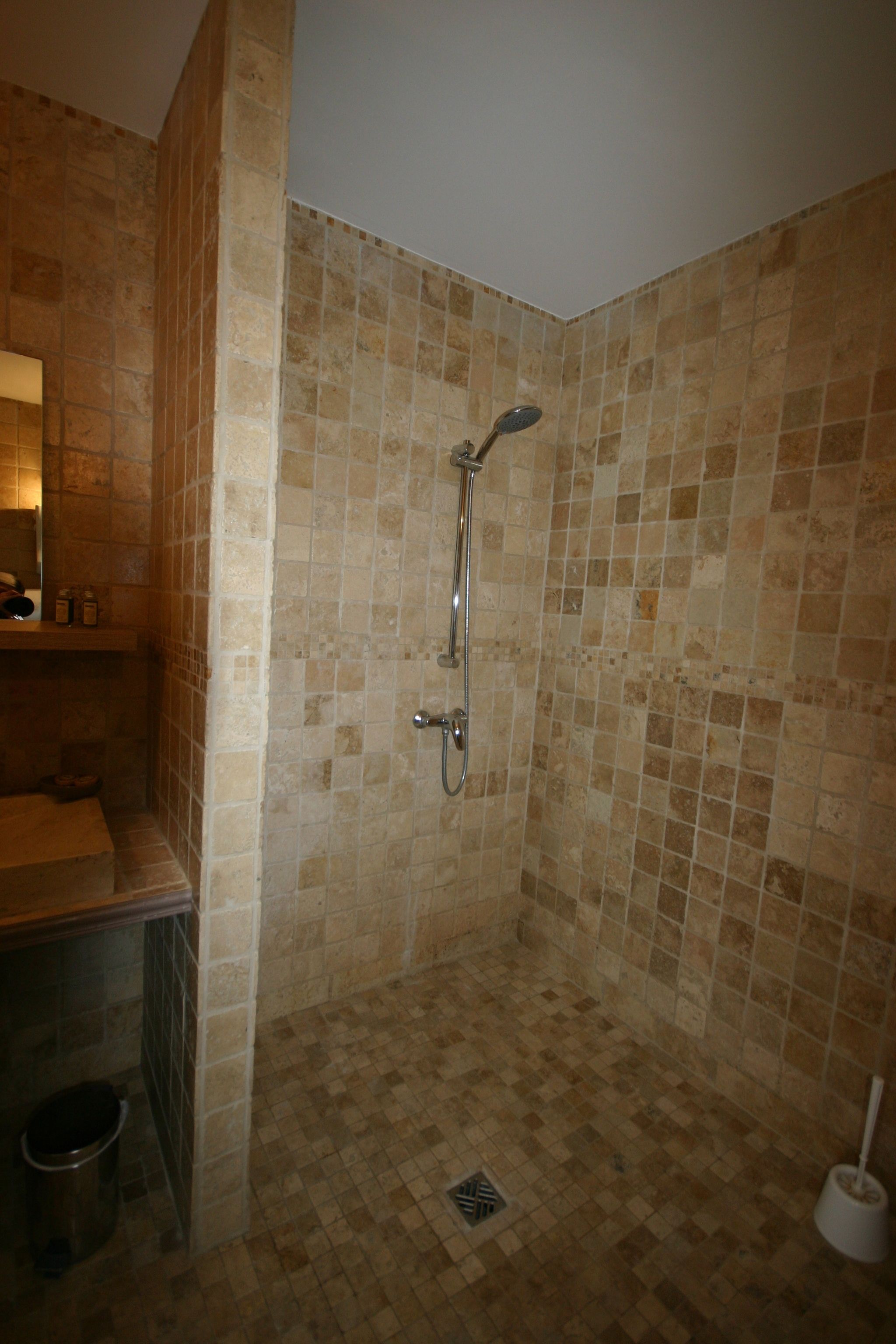 A bathroom with a shower, tiled walls, a sink, and a trash bin.