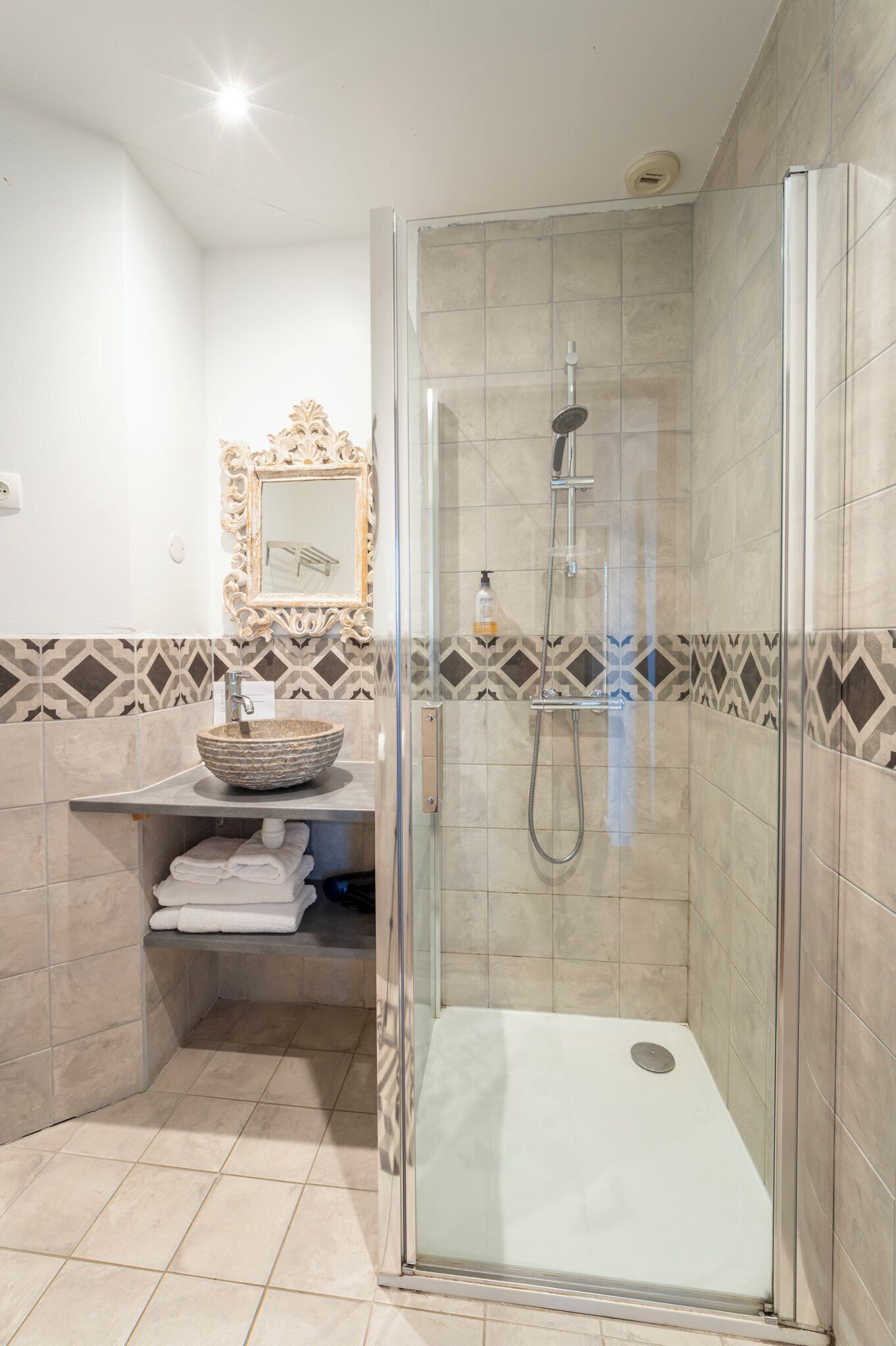 Un baño moderno con ducha envuelta en vidrio, tocador con lavamanos decorativo y azulejos estampados en las paredes.