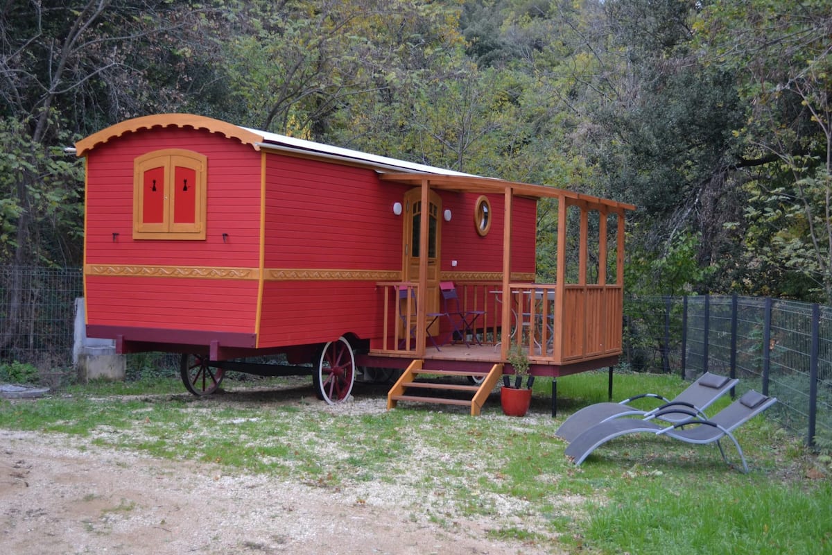 A red and yellow wooden house with a porch, a small deck, and a fenced garden area with two lounge chairs.