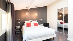 Een moderne slaapkamer met een groot bed, nachtkastjes, een spiegel en uitzicht op de kamer via een schuifdeur.