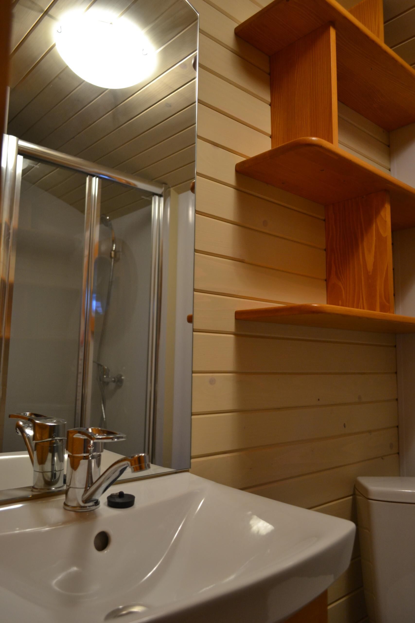 Een badkamer met een witte wastafel, een spiegel, een douche en houten planken.