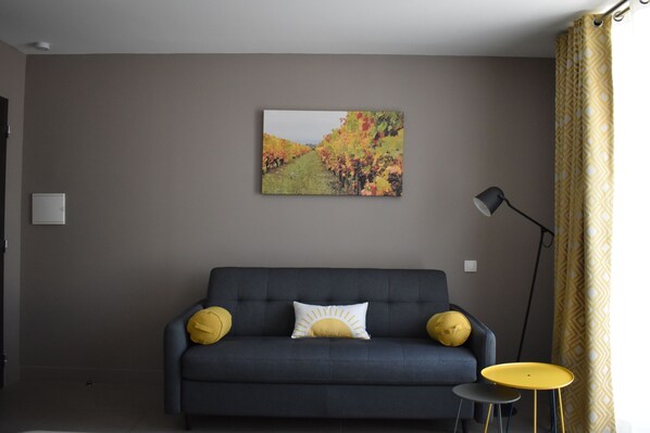A living room with a dark blue sofa, two yellow pillows, a white pillow with a sun design, a small round yellow table, and a floor lamp. - Coeur de Vignes (Saint-Peray)