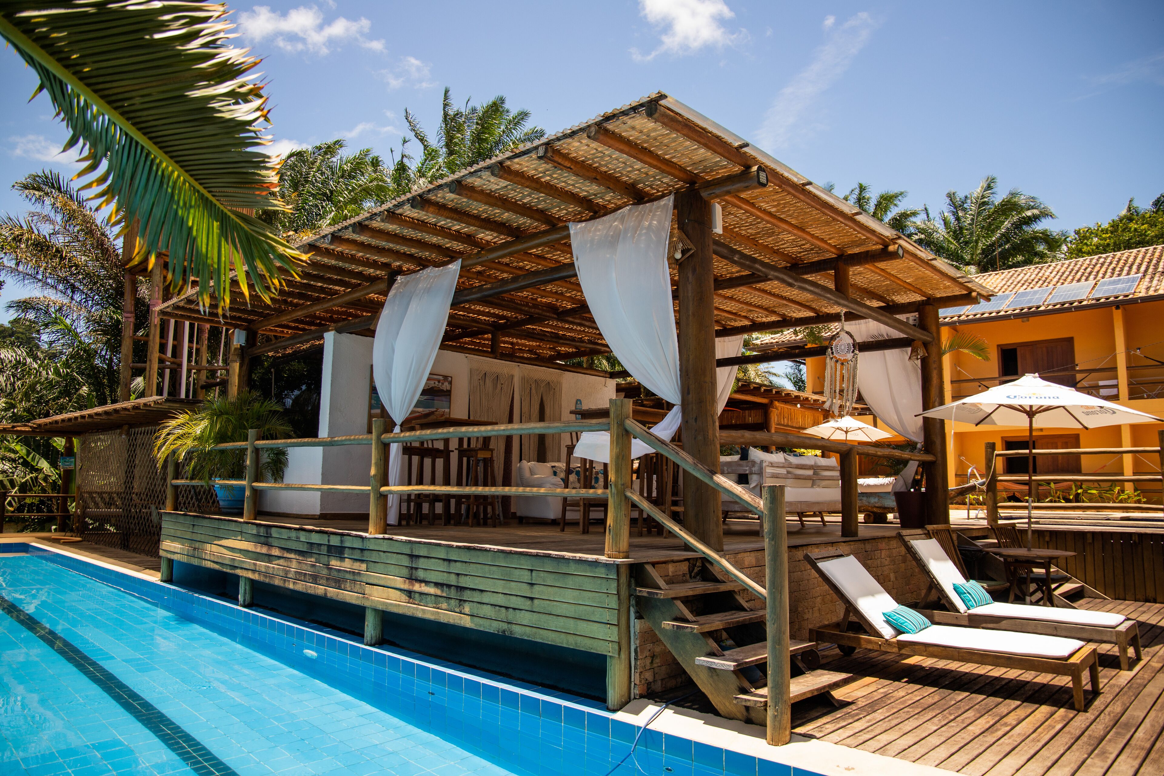 Un espace aménagé au bord de la piscine, avec une terrasse en bois, des chaises longues et un coin salon couvert équipé de parasols.
