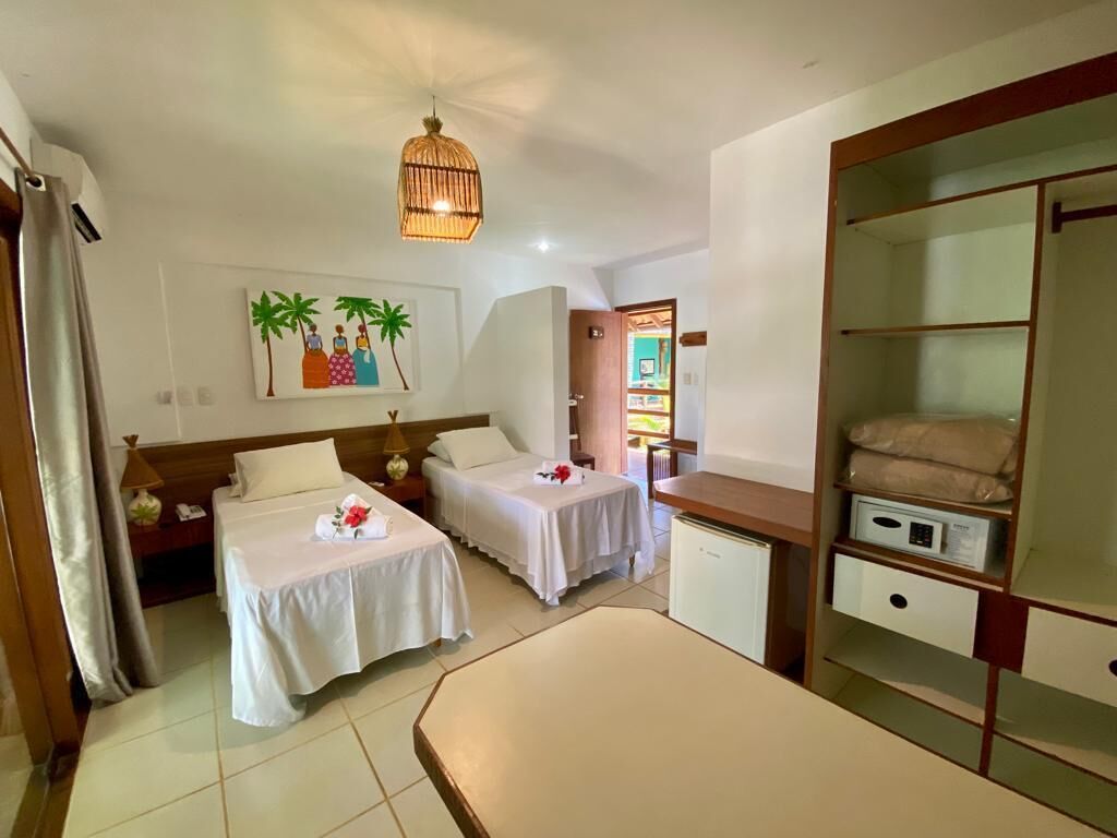 A hotel room with two beds, a small desk, a wardrobe, and a painting on the wall.