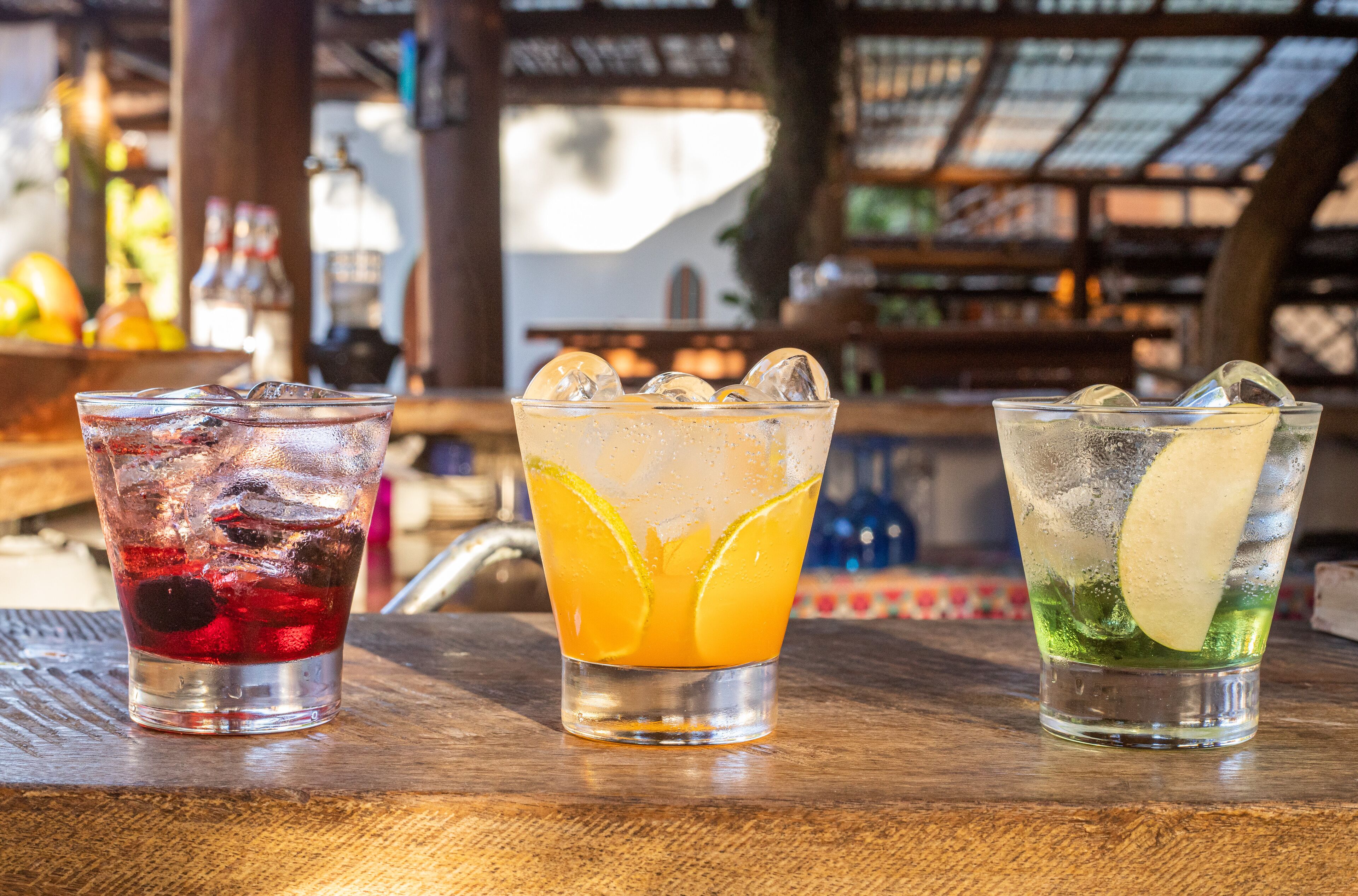 Tres vasos de bebidas sobre una barra de madera.