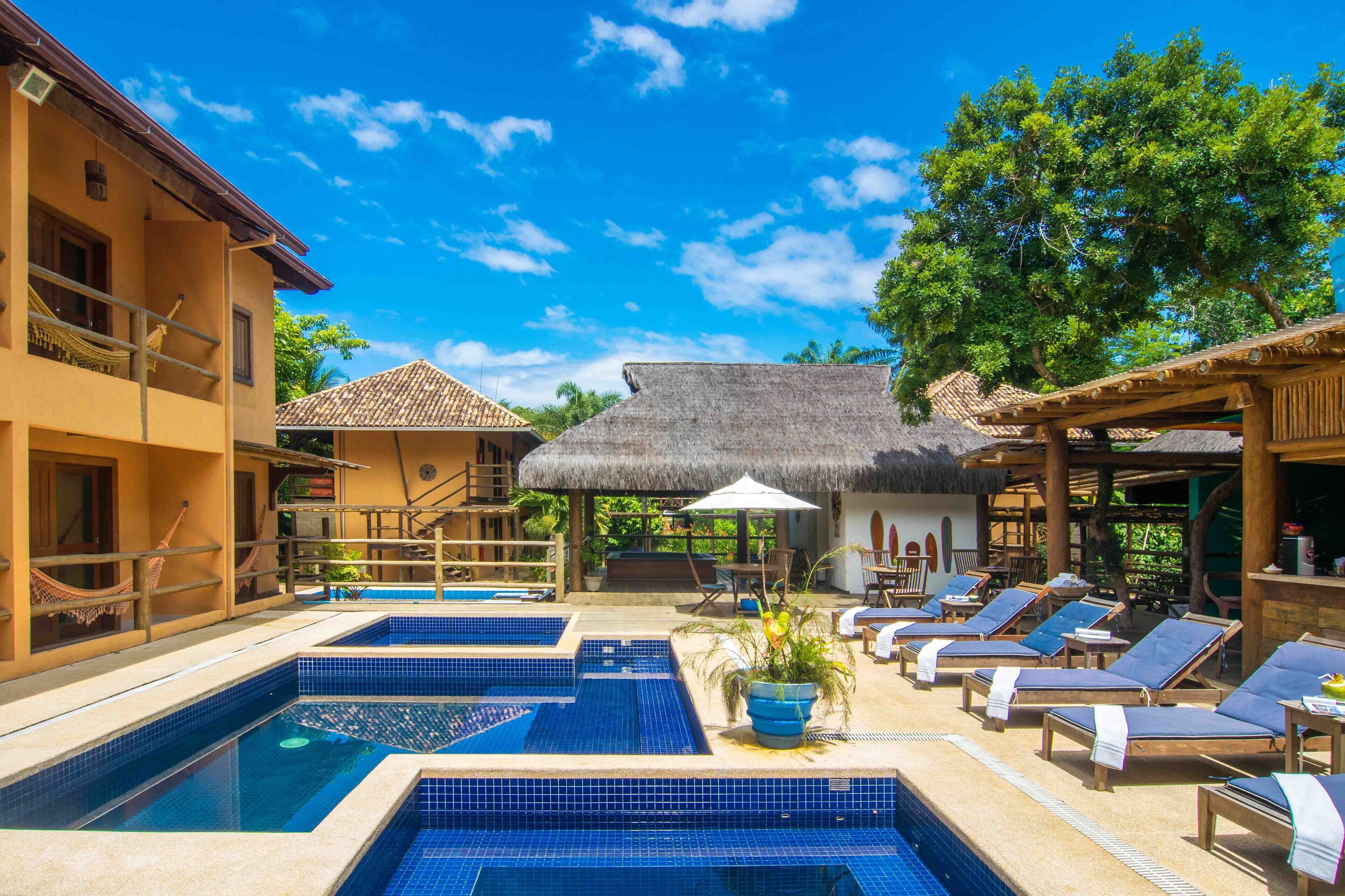 A pool area with multiple swimming pools, lounge chairs, and a thatched-roof structure.