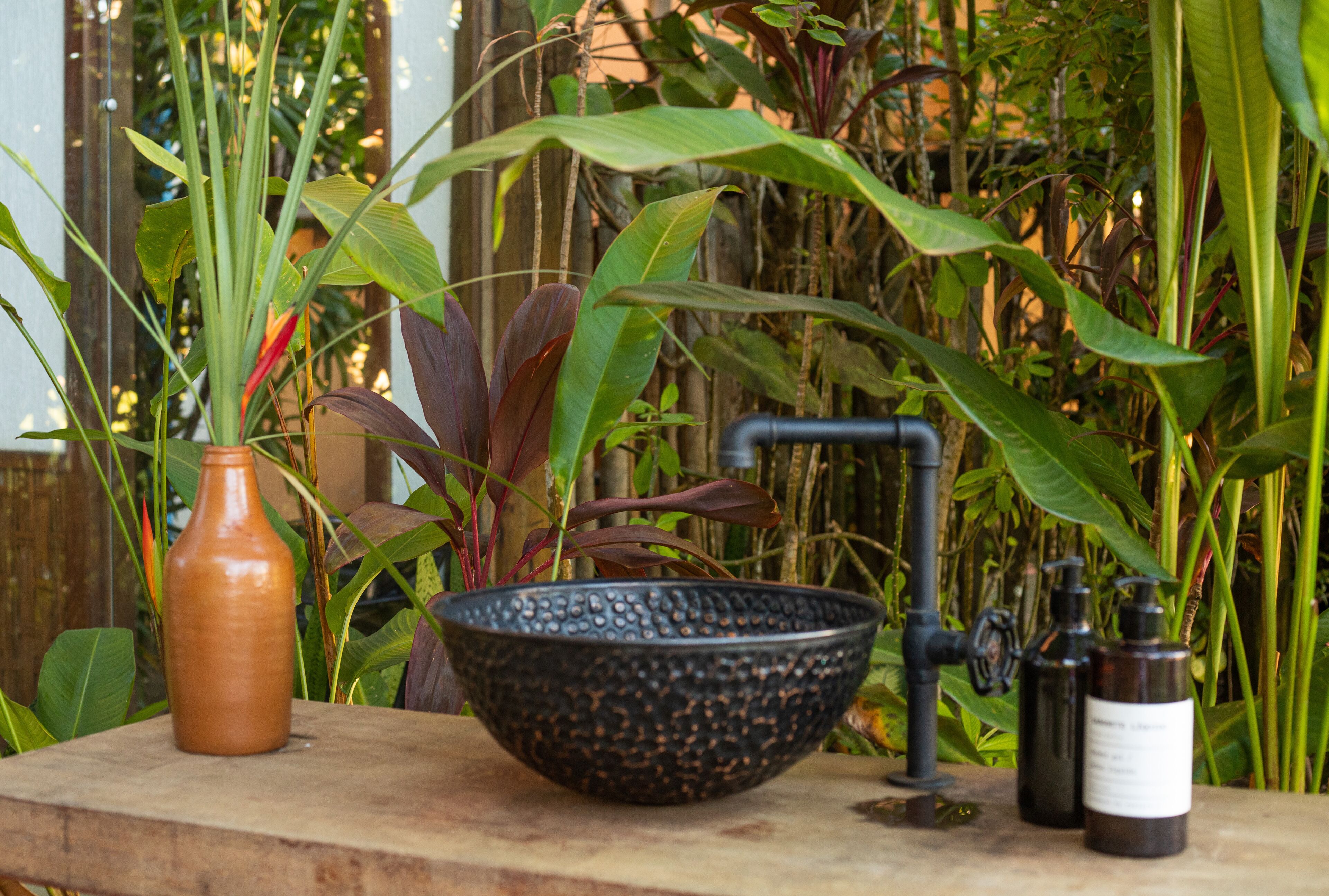 A rustic outdoor setting with a large black bowl, a brown vase, and two dark bottles on a wooden surface.