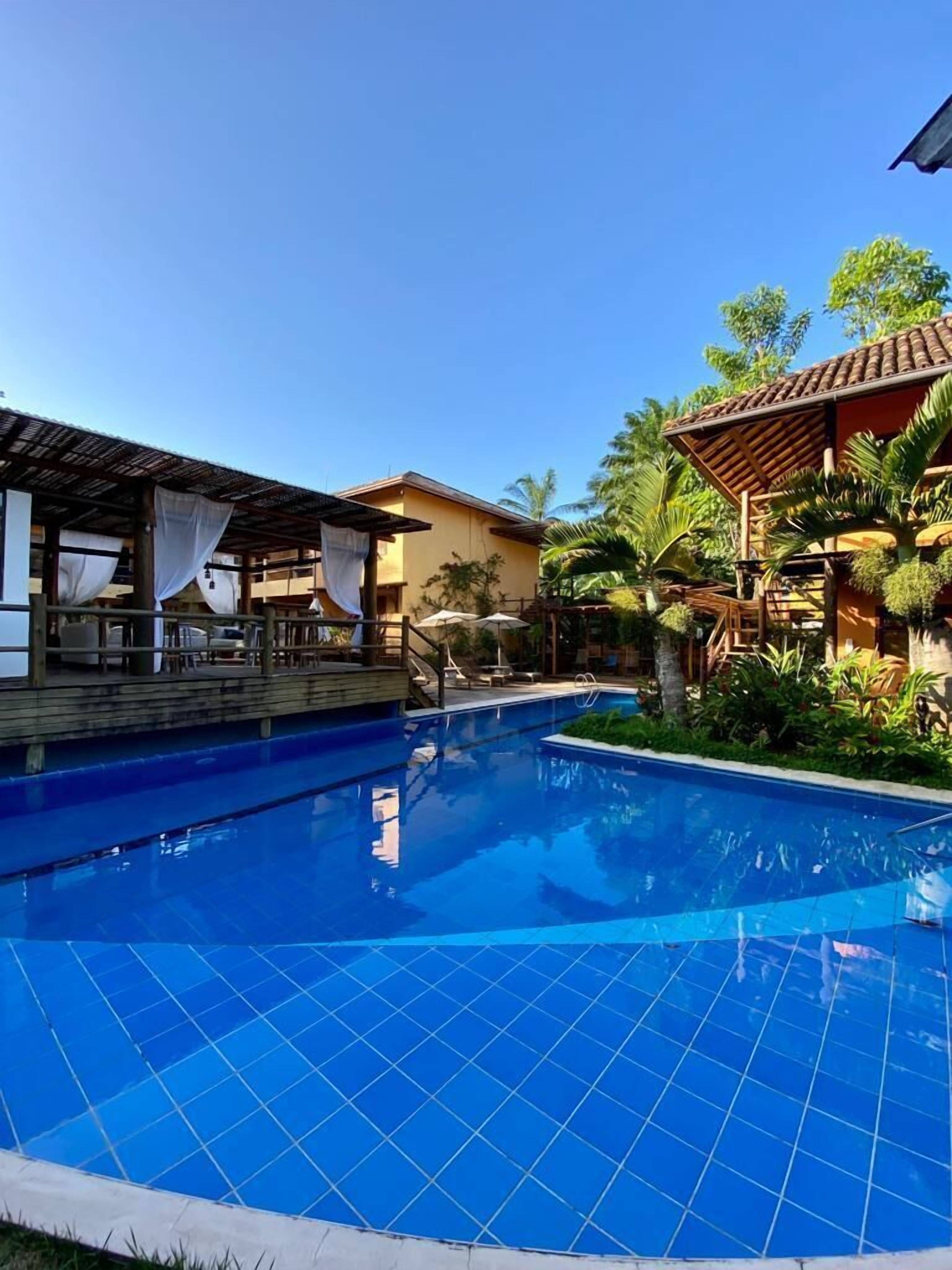 A swimming pool with tiled edges, surrounded by lounge areas with umbrellas, and tropical plants.