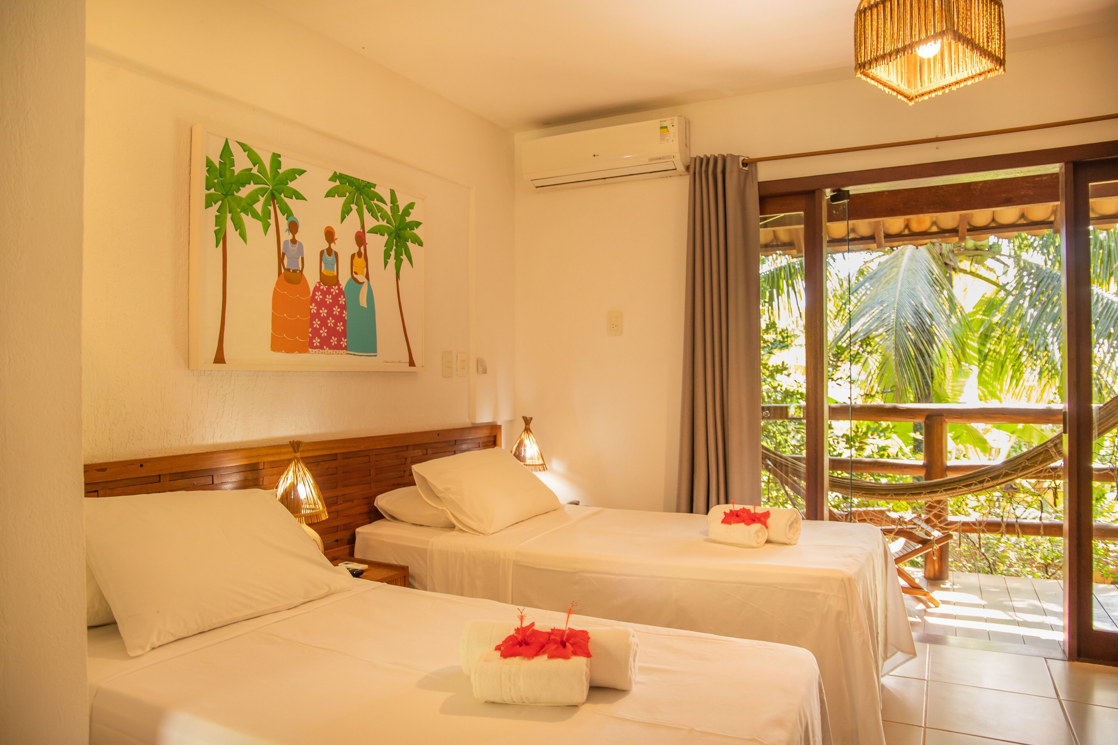 A hotel room with two beds, a painting of palm trees, an air conditioning unit, and a view of greenery through a window.