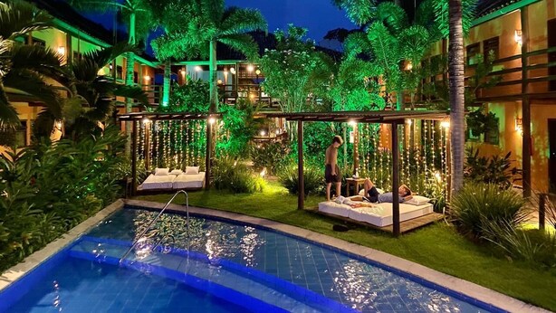 A pool area with a hot tub, lounge chairs, and a pergola with string lights.