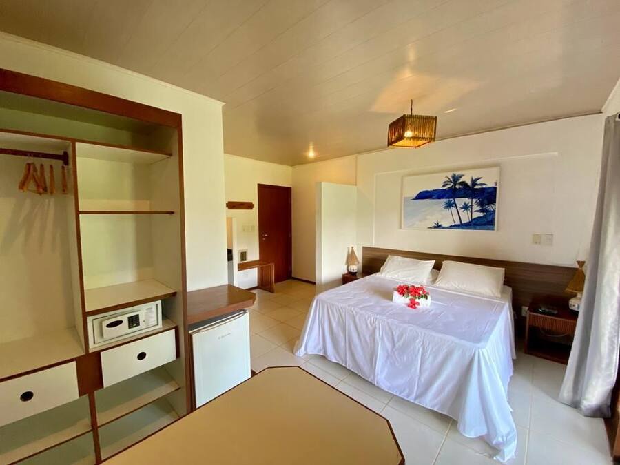 Quarto de hotel com cama, escrivaninha, guarda-roupa e um quadro na parede.