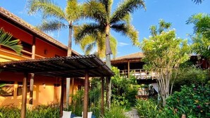 A tropical garden with a bed under a pergola, surrounded by palm trees and lush greenery.