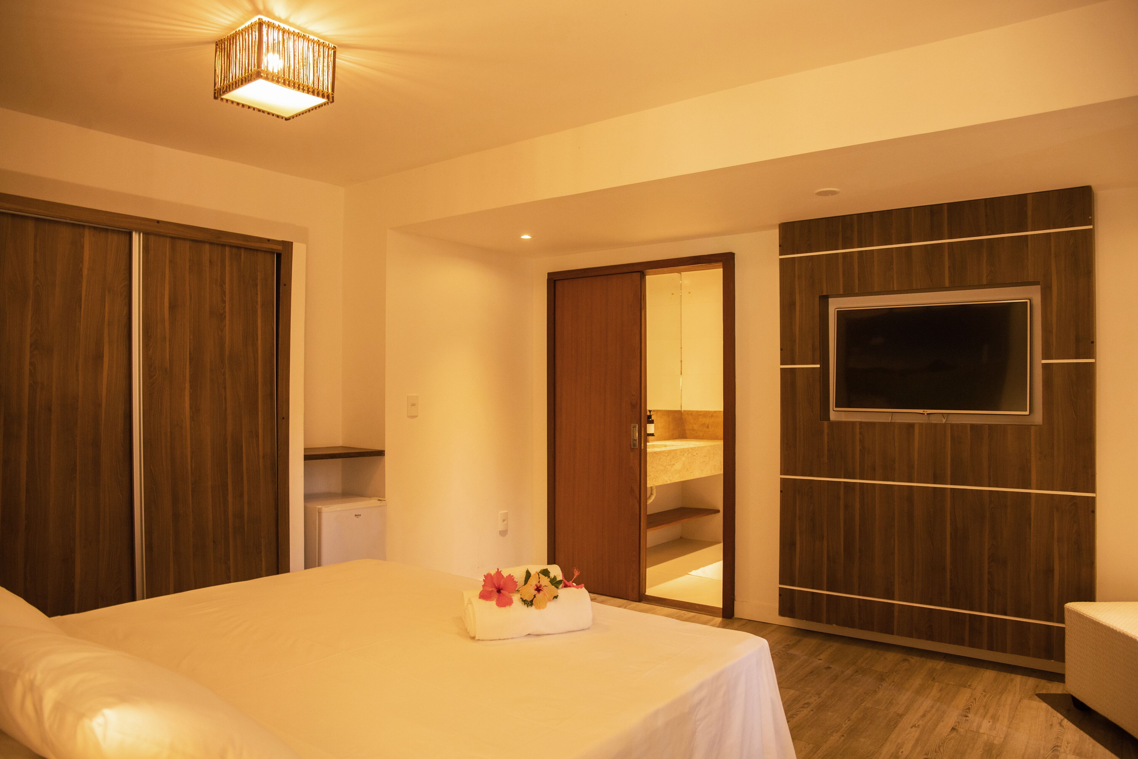 Une chambre d’hôtel avec un lit, un téléviseur fixé au mur, une armoire en bois et une petite kitchenette.