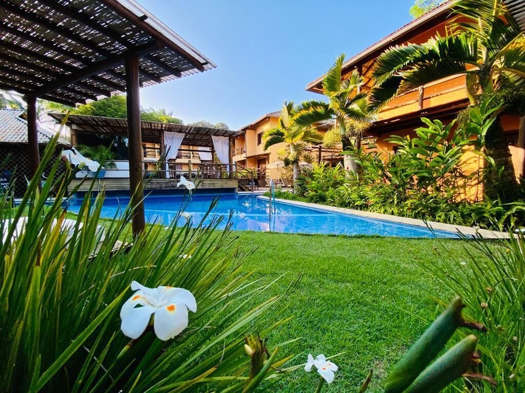 A pool area with a clear blue pool, surrounded by lush green grass and tropical plants.