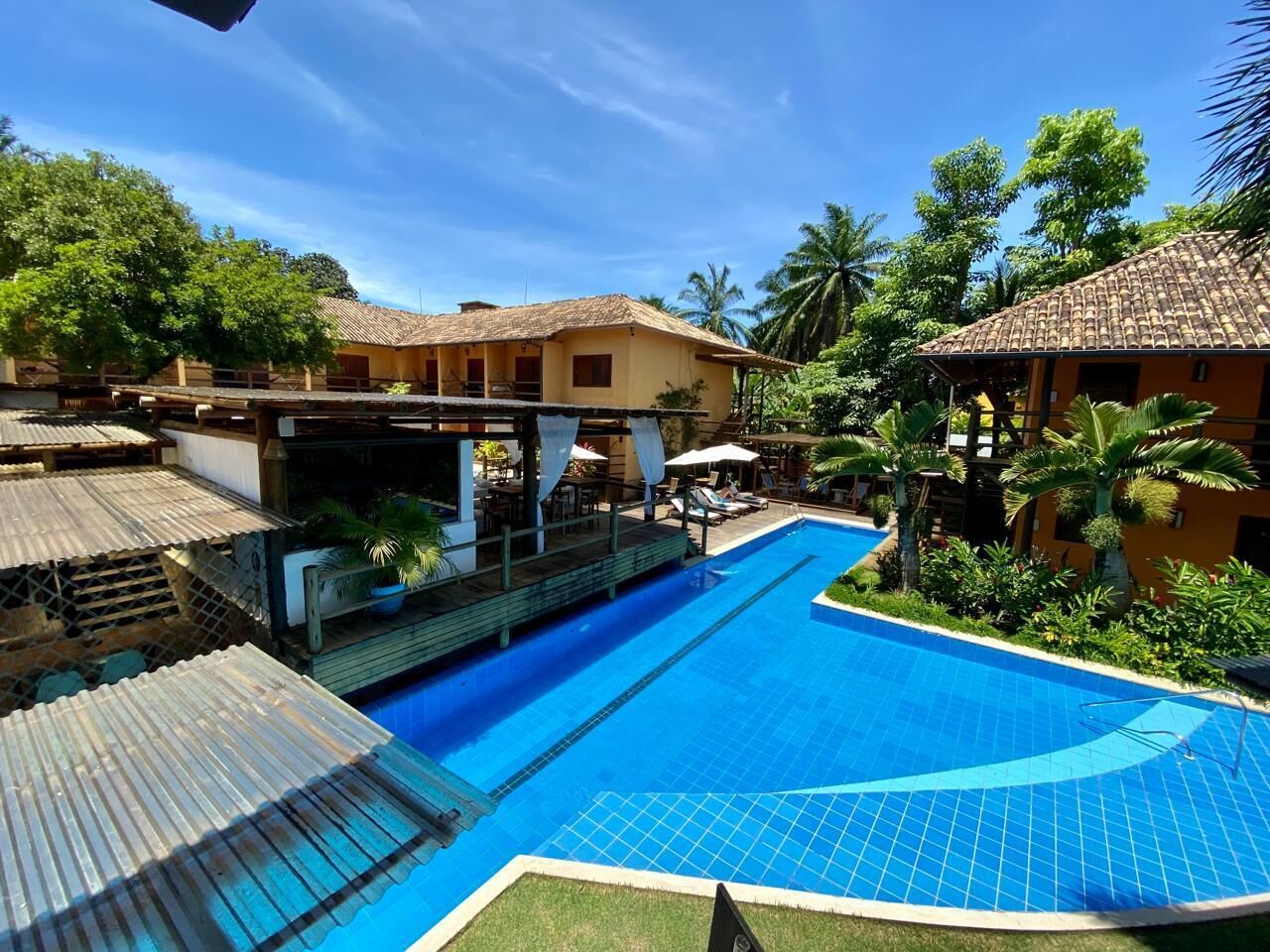 Une piscine dotée d’une terrasse carrelée, entourée de bâtiments aux toits couverts de tuiles et de palmiers.
