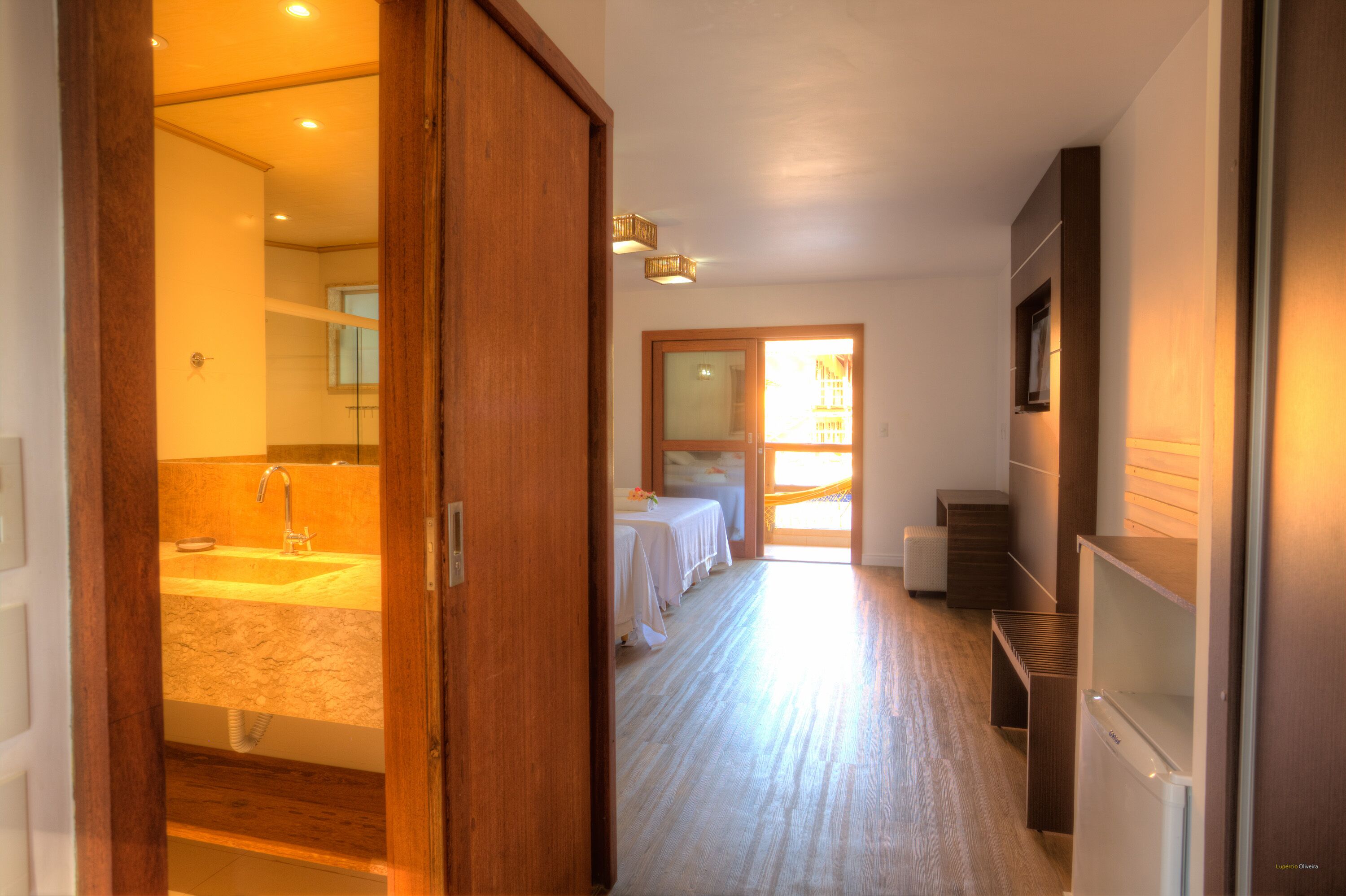 A hotel room with a bathroom, a bed, a desk, and a refrigerator.