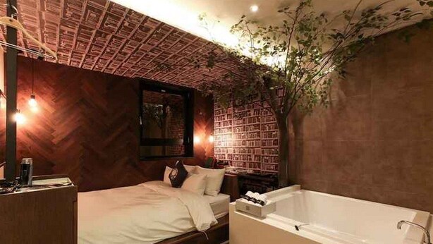 A bedroom with a bed, a nightstand, a large window, and a wall of bookshelves. - Sota Stay Gundae (Seoul)