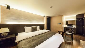 Habitación de hotel con cama, mesita de noche, lámpara, escritorio, silla y espejo.