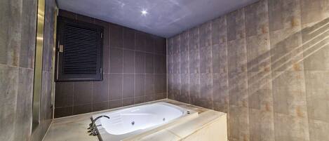 A modern bathroom with a freestanding bathtub, dark tiled walls, and a recessed ceiling light.