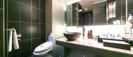 A modern bathroom with dark tiles, a white toilet, a large mirror, and a bowl sink.