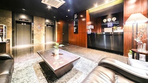 Un vestíbulo de hotel con una recepción, dos ascensores, una mesa de centro y asientos de cuero.