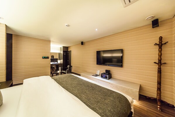 Habitación de hotel con cama, televisor montado en la pared, suelo de madera y un pequeño escritorio con silla.
