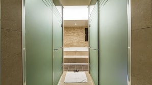 Un pasillo estrecho con puertas de vidrio que dan a un baño con bañera y una toalla en el suelo.