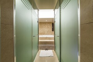 Un pasillo estrecho con puertas de vidrio que dan a un baño con bañera y una toalla en el suelo.