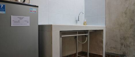 Un baño pequeño con lavamanos, ducha y refrigerador.