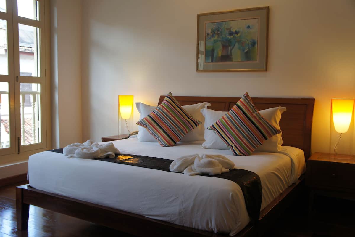 A neatly made bed with white linens and striped pillows, a painting on the wall, and bedside lamps.