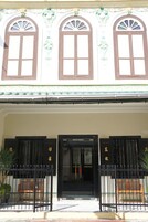 Un edificio con tres ventanas arqueadas, un portón negro y un banco de madera en el exterior.
