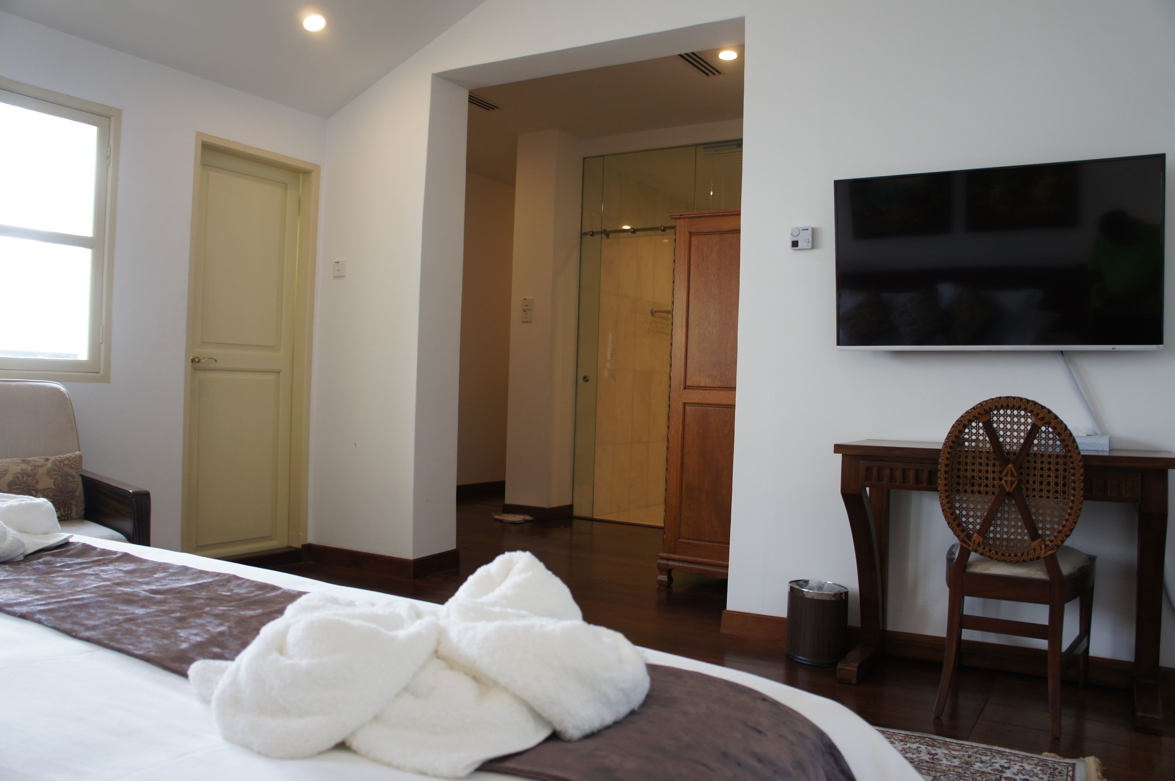 A hotel room with a bed, a desk, a chair, a TV, and a bathroom visible through an open door.
