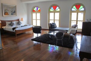 Habitación de hotel con cama, una silla, una mesa y dos ventanas con vidrieras.