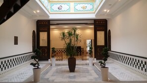 A grand entrance with a tiled floor, two large potted plants, and a central pillar.